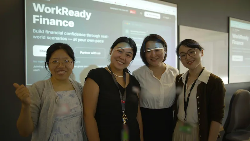 Four people smiling in front of a projection of the WorkReady Finance homepage.